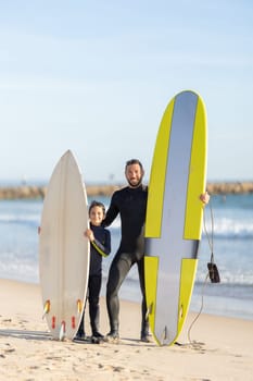 A family of surfers - father and son standing on the seashore with their surfing boards. Mid shot