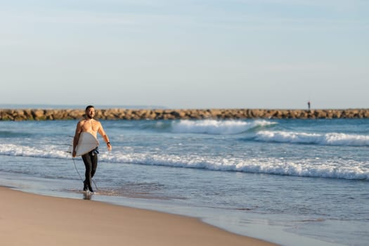 A man surfer with naked torso walking on the seashore. Mid shot