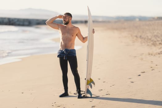 An athletic man surfer with naked torso looking in the distance. Mid shot