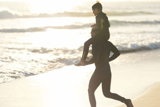 Little son on the shoulders of his father running to the sea at sunset. Mid shot