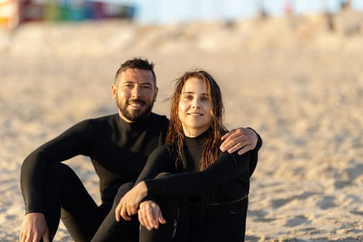 A couple of man and woman surfers sitting on the seashore. Mid shot
