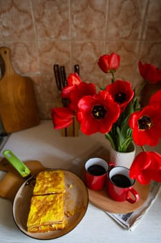 Red cup with hot coffee on the background of the kitchen. Delicious toasts with egg lie on a frying pan. Vase with red poppies, coffee break