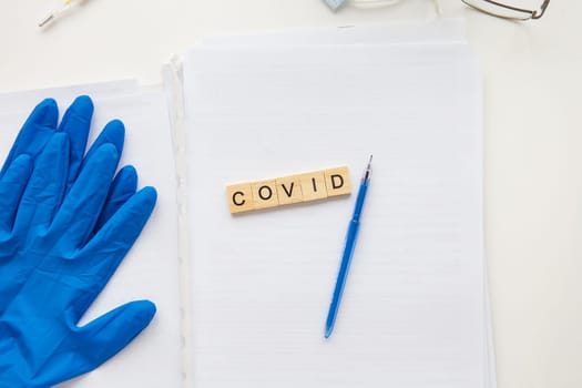 The inscription covid on a medical background, next to gloves, a pen, glasses and papers with patient data. Medical theme. Concept: vaccination against coronavirus