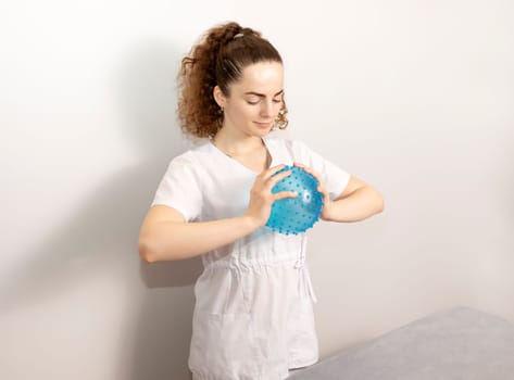 Female Rehabilitation Specialist, Physiotherapist In White Medical Clothes Holds Massage Ball With Pimples In Therapeutic Cabinet. Health Specialist, Rehabilitation. Horizontal. High quality photo