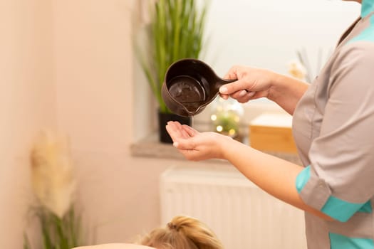 Masseur pours warm lotion, oil from pottery on hand before starting massage, kneading muscles of client in spa salon. Mental, health sustainability. Relaxation, healthcare. Horizontal plane