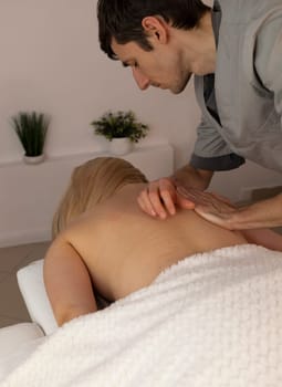 Male masseur, therapist stretches back of white woman, client during professional therapeutic massage in spa salon. Fascia stretching. Mental, health sustainability. Relaxation, healthcare. Vertical.
