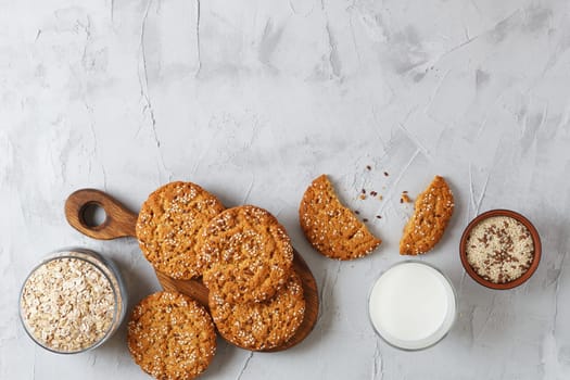 Oatmeal cookies with sesame seeds and flax seeds on a gray background with a jar of oatmeal and a glass of milk.Copy space