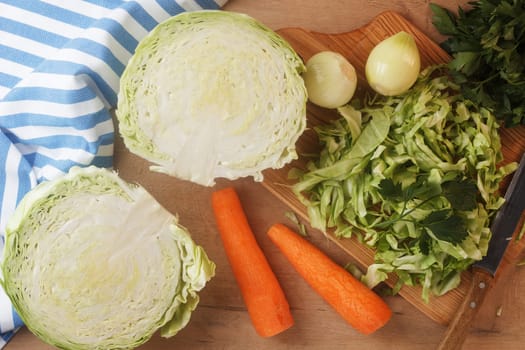 Sliced cabbage on a wooden board with carrots, onions and herbs. Preparing to cook coleslaw