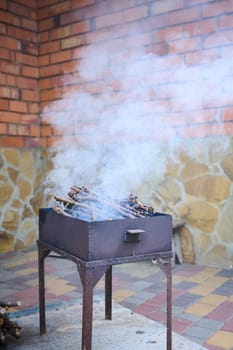 BBQ grill with flaming charcoal and smoke, in the backyard against red wall bricks background. The concept of summer picnic and barbecue party