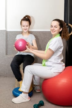 Smiling Child, Teenage Girl With Disability Does Physical Exercises With Support Of Rehabilitation Specialist, Physical Therapist. Rehabilitation. Musculoskeletal Disorder. Vertical plane.