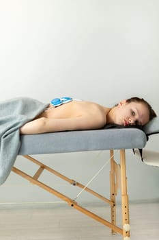 Caucasian Young Woman With Cerebral Palsy, Scoliosis Lying on Couch, Getting Wireless Electric Muscle Stimulator Massage. Pain Treatment. Rehabilitation, Medical Equipment. Vertical plane.