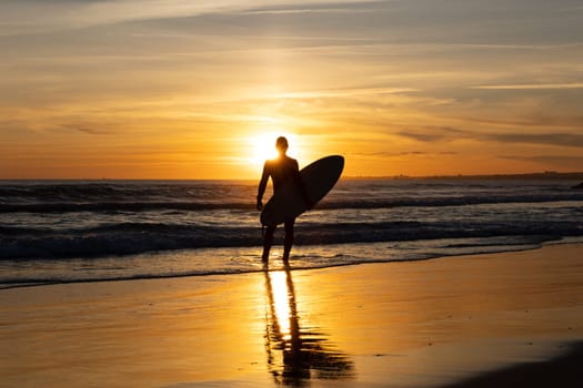 Silhouette of a man surfer holding surfboard standing alone on the seashore. Mid shot