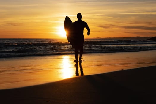 Silhouette of a man surfer walking out on the seashore at sunset. Mid shot