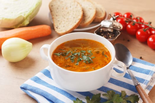 Vegetable soup with potatoes, cabbage, carrots and onions in a white bowl on the kitchen table with cereal bread. Vegetarian food.