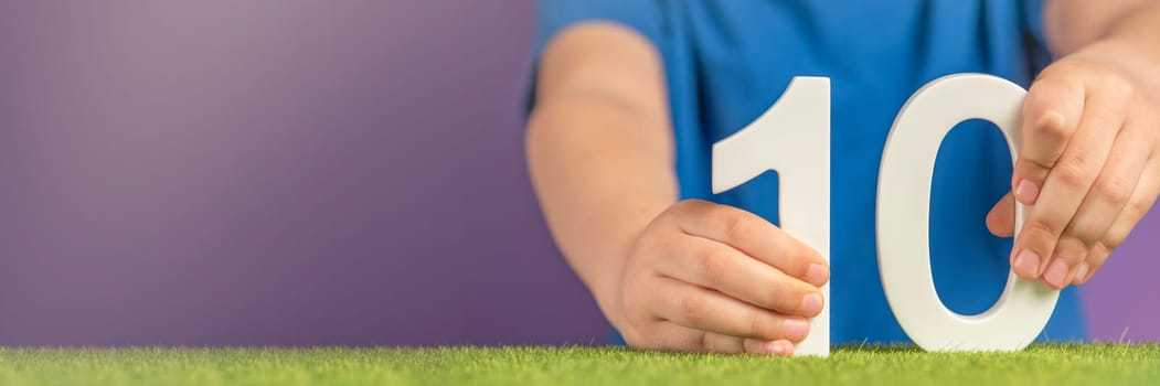 Number 10 in hand. The hand holds a white number ten on a purple background, 10 percent per annum. Advertising banner or greeting card. Concept for World Science Day, November 10th