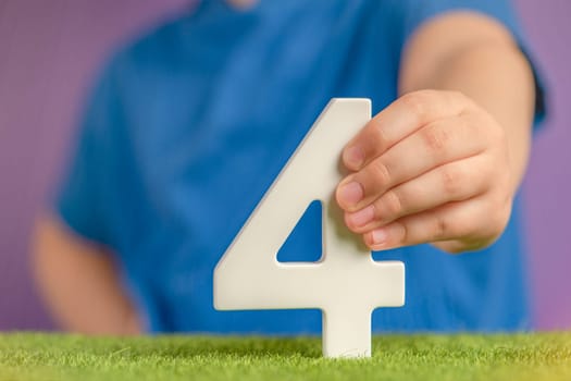 Number 4 in hand. Hand holding white number four over green grass and purple background, birthday concept, competition place, four percent per annum. USA Independence Day, 4 July.
