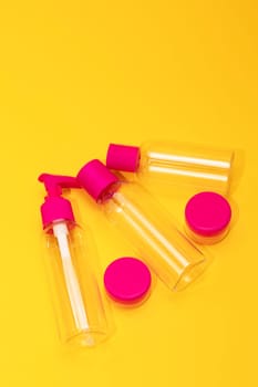 Top view travel bottle kit for liquids, cream. Toiletries Beauty Kit on yellow orange background. Airplane approved luggage reusable container size. Summer time, vacation. Vertical. Copy space.