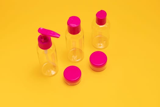 Cosmetic plastic clear fuchsia travel bottle kit for soap, cream, shampoo, gel, lotion, liquids. Toiletries Beauty Kit on yellow orange background. Airplane approved luggage container size. Copy space