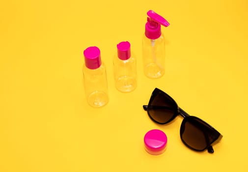 Airplane luggage fuchsia bottle container size with sun glasses on yellow orange background. Transparent travel toiletries beauty kit. Vacation summertime concept, , copy space. Horizontal plane