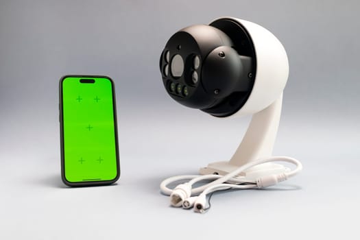 Surveillance IP Wireless Camera, Chroma Key Green Screen of Smartphone On Gray Background. Security Equipment For Smart Home with Online Remote App Monitoring, Control. Horizontal plane, mockup.