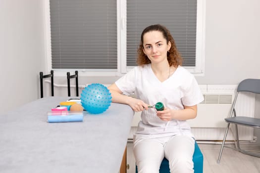 Rehabilitation Specialist, Physical Therapist With Rehab Tools, Foam Roller, Lacrosse Ball, Massage Ball With Pimples, Mesoroller With Titanium Needles, Kinesiology Tape On Couch in Therapeutic Room.