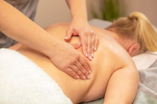 Masseur, therapist doing professional therapeutic massage on back of overweight woman, kneading muscles of client in spa salon. Mental, health sustainability. Relaxation, healthcare. Horizontal plane