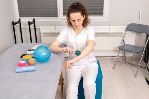 Rehabilitation Specialist, Physical Therapist With Rehab Tools, Foam Roller,Massage Ball With Pimples, Mesoroller With Titanium Needles, Kinesiology Tape On Couch in Therapeutic Room. Horizontal plane
