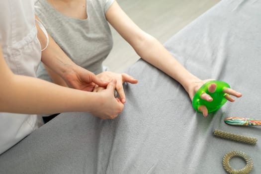 Unrecognizable Doctor Neurologist Stretches Fingers Of Female Young Girl with Disability. Physical Therapy Equipment, Health Specialist, Rehabilitation. Horizontal plane.