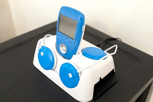 Closeup Blue Wireless Electric Muscle Stimulator, Pain Treatment on Shelf. Charging Rehabilitation and Training Tool, Equipment. Healthcare and Medical concept. Horizontal plane. High quality photo
