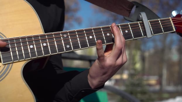 A young man plays the guitar in nature. The student masterfully plays the guitar and quickly plucks the strings. 4k