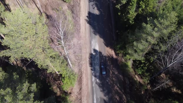 The car is driving along a forest road. One car overtakes another on the road in the middle of the fir trees. Aero filming from a drone. 4k