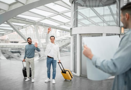 Meet And Greet Service. Guy Meeting His Travelers Friends Holding Paper Sign At Modern Airport Arrival Terminal Indoors. Transportation And Business Travel. Selective Focus On Joyful Tourists