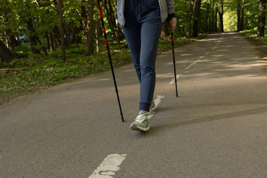 Woman's Legs Trekking With Sticks, Step Along The Path In Park, Cropped Hiking Female, Nordic Walking With Sticks, Cross-country Running. Horizontal Plane. High quality photo