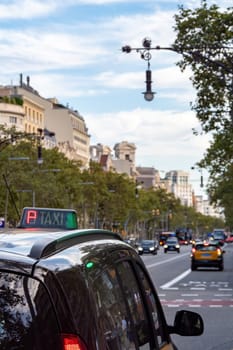 Taxi stands at the traffic light or waits for a passenger on the street of Barcelona. Selective focis. View to Passeig de Gracia.