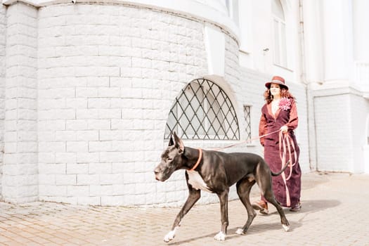 A photo of a woman and her Great Dane walking through a town, taking in the sights and sounds of the urban environment.