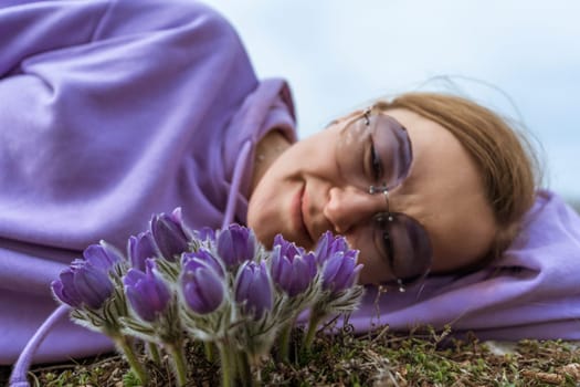 Dream grass woman spring flower. Woman lies on the ground and hugs flowers pasqueflower or Pulsatilla Grandis flowers.