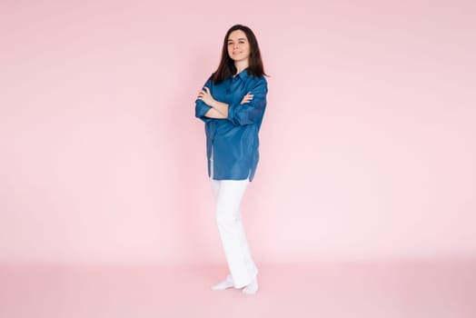 Portrait of professional businesswoman in smart casual attire standing confidently with folded hands, isolated on a pink background.