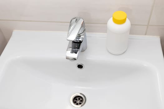 Plumber drain granules in White Plastic Bottle With Yellow Cap On Bathroom Sink In Shower Room. Clog Cleaner, Housework Help. Cleaning enzymes, Prevention of Blockages In Traps. Horizontal plane.