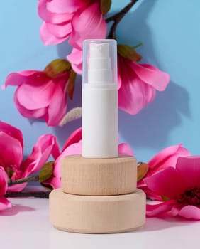 White plastic bottle with a dispenser for cosmetics on a blue background with pink flowers. Container for creams, lotion