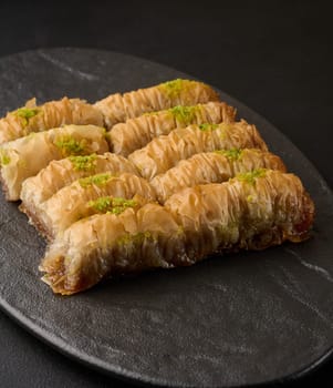 Pieces of baked baklava in honey and sprinkled with pistachios on a black board