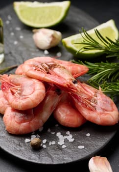 Boiled shrimp on a board, lemon slices, spices on a black background