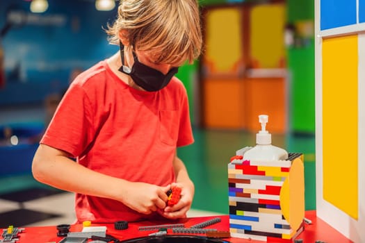 A boy in a medical mask plays with a constructor. child playing and building with colorful plastic bricks table. Early learning and development.