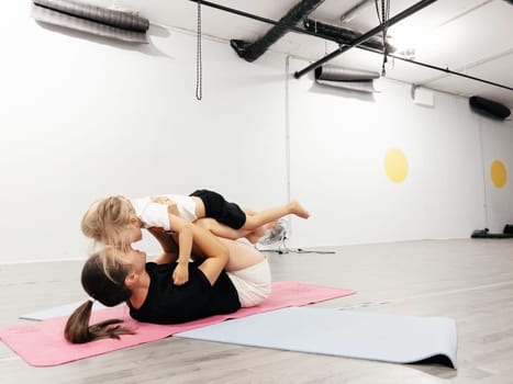 Mom holds a little girl on bent legs lying on a mat in the gym. High quality photo