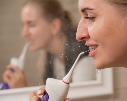 A woman with braces on her teeth uses an irrigator. Close-up portrait