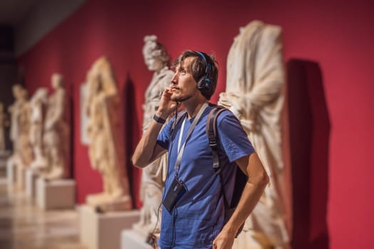 Portrait of contemporary man looking at sculptures and listening to audio guide at museum exhibition.
