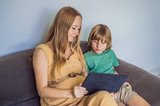 pregnant mom and son look at the tablet. Reading a book or watching a cartoon or making a video call. Look at the photo from the ultrasound.