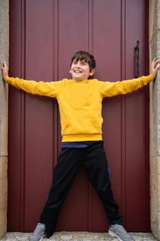 Smiling young boy standing with opened arms and legs in a door entrance, having fun.