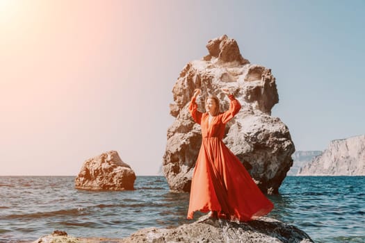 Woman travel sea. Young Happy woman in a long red dress posing on a beach near the sea on background of volcanic rocks, like in Iceland, sharing travel adventure journey