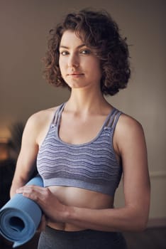 A day without yoga is a day wasted. Cropped portrait of an attractive young woman standing alone and holding her yoga mat before an indoor yoga session