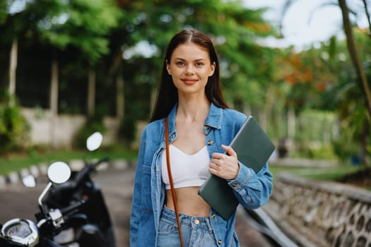 Woman smiling walking in the park outside with laptop freelancer against a backdrop of green palm trees in summer, tropical backdrop, blogger on a trip, work online. High quality photo